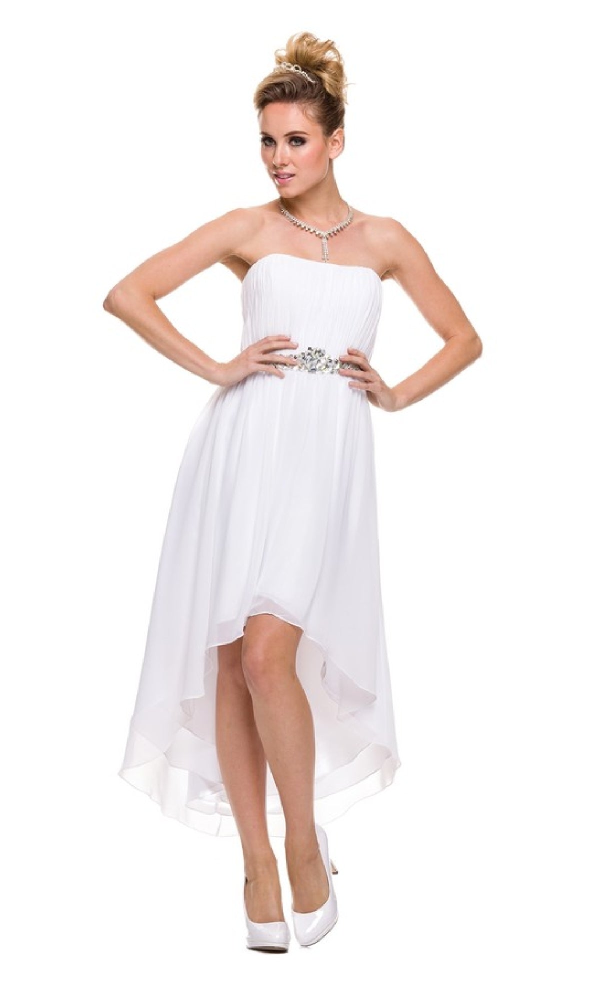 A woman poses with her hands on her hips against a white background, wearing the Juliet 747 High-Low Semi-Formal Dress in white, featuring a strapless design and embellished waistline, paired with white heels and a necklace.